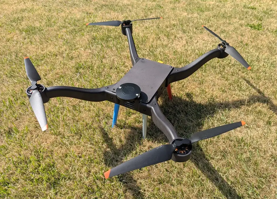 A finished black quadcopter drone with a payload module on its body, standing on grass.